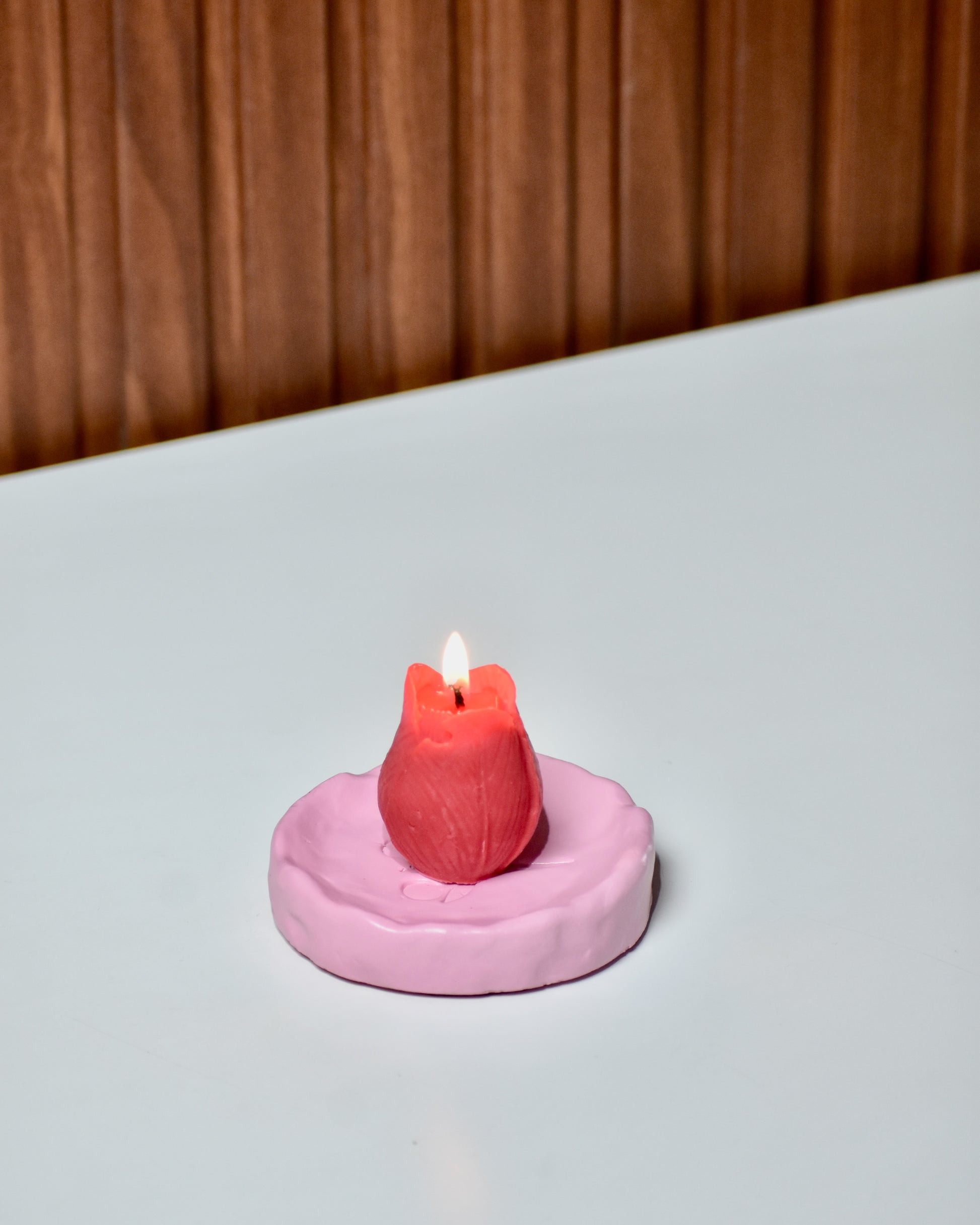 Pink concrete burner base with a red floral candle on a white surface.
